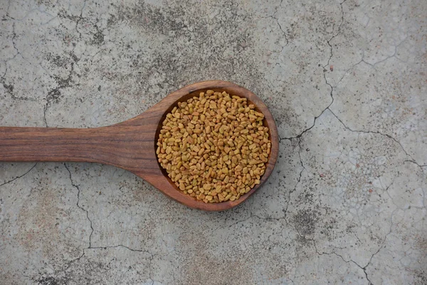 フェヌギリシャの種子で木製スプーンで割れたコンクリートテクスチャの背景 — ストック写真