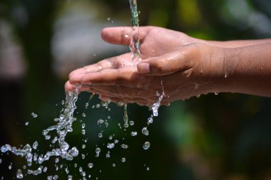 İki eliyle doğaya su döken bir çocuk. Su sıçratan eller.