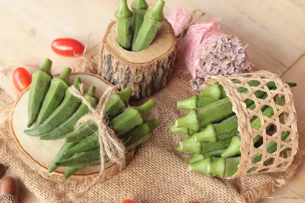 Vainas de okra frescas y rebanadas sobre fondo de madera — Foto de Stock