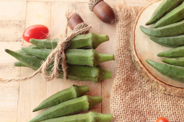 Vainas de okra frescas y rebanadas sobre fondo de madera — Foto de Stock