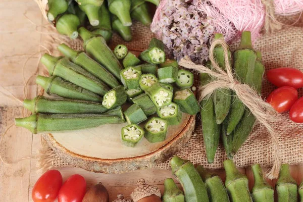 Vainas de okra frescas y rebanadas sobre fondo de madera — Foto de Stock