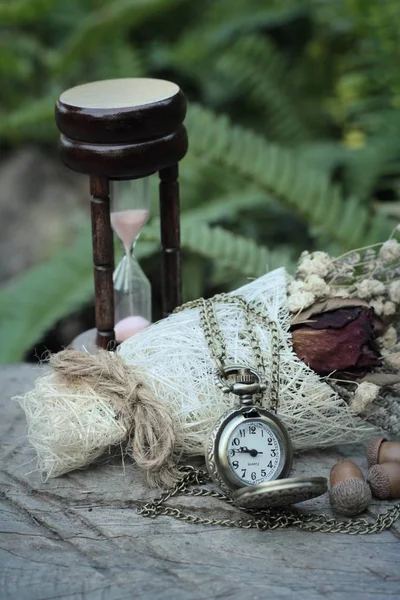 Antique pocket watch and hourglass with dried flowers.