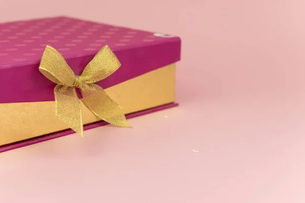 Caja de regalo púrpura con lazo de cinta dorada sobre fondo rosa. milimalismo. Ventas, compras, Navidad invierno y cumpleaños vacaciones concepto —  Fotos de Stock