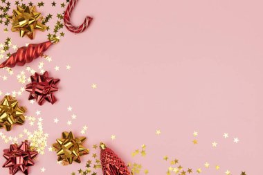 Noel kırmızı ve altın işlemeli, fiyonklu ve oyuncak Noel sarkıtları, yıldız konfetileri ve pastel pembe arka planda fotokopi alanı olan bir şeker kamışı. Tasarımınız için yaratıcı konsept