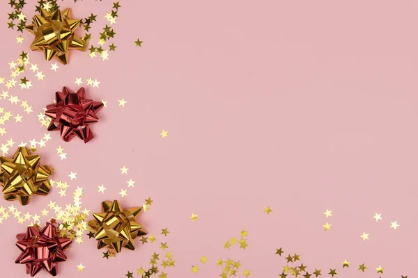 Yaratıcı kırmızı ve altın renginde fiyonklu ve pastel pembe arka planda yıldız konfetisi. Tasarımın için yaratıcı bir konsept. Düğün, doğum günü, Noel tebrik kartı
