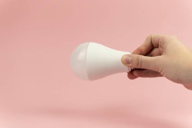 Kadınlarda enerji tasarrufu ampulü pembe arka planda. Yakın plan. Enerji tasarrufu kavramı