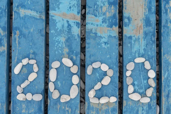 2020 escrito en una línea de piedras sobre un fondo de madera. El pavimento de madera azul hecho de tablas en la orilla del mar. naturaleza año nuevo tarjeta concepto . Fotos de stock