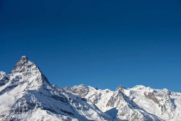 Montañas de invierno con nieve y cielo azul en buen día de sol. Estación de esquí y concepto deportivo. Montañas del Cáucaso, región Dombay. Vista desde la parte superior de Musa Achitara, espacio de copia, moc up Imagen de stock