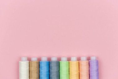 Bobinin pembe arkaplandaki çok renkli iplikleri. Dikiş malzemeleri, desenler ve aksesuarlar. Dikiş, dikiş, nakış. Metin için boşluk. düz yat.