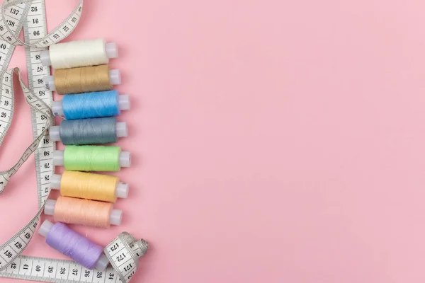 Bobinin çok renkli iplikleri ve pembe arka planda santimetre. Dikiş malzemeleri, desenler ve aksesuarlar. Dikiş, dikiş, nakış. Metin için boşluk. düz yat.