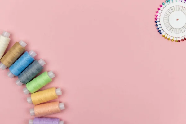 Bobinin çok renkli iplikleri, pembe arka planda iğneler. Dikiş malzemeleri, desenler ve aksesuarlar. Dikiş, dikiş, nakış. Metin için boşluk. düz yat.