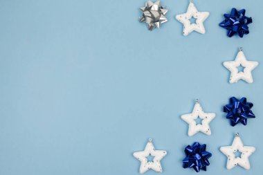Tatil süslemeleri. Beyaz yıldızlardan oluşan yaratıcı kompozisyon - Noel ağacı oyuncakları, açık mavi arka planda klasik mavi ve gümüş fiyonklar. Üst manzara, yakın çekim. Boşluğu kopyala