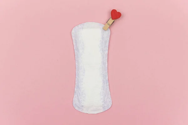 Білий щоденний менструальний жіночий простір для гігієни або періоду крові з червоною шпилькою з серцем як символ любові до тіла. Концепція продуктів жіночої гігієни інтимного періоду. Копіювати простір, рожевий фон — стокове фото