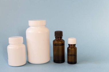 Haplar için beyaz şişeler ve mavi arka planda gerekli yağlar için cam şişeler. Tıbbi, eczane ve sağlık konsepti... Boşluğu kopyala