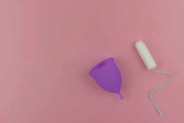 Copa menstrual rosa y un tampón sobre fondo violeta pastel. Producto alternativo de higiene femenina durante el período. Menstruación, protección, concepto de comparación, espacio para copiar, vista superior — Foto de Stock