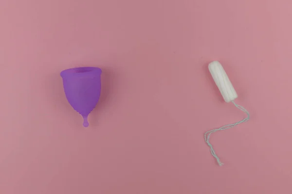 Xícara menstrual rosa e um tampoo em fundo violeta pastel. Produto de higiene feminino alternativo durante o período. Menstruação, proteção, conceito de comparação, flat lay, vista superior — Fotografia de Stock