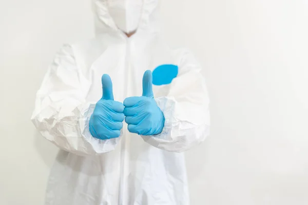 Doctor en traje protector blanco, máscara médica y guantes azules muestra un pulgar hacia arriba. Epidemia, pandemia de coronavirus covid 19. Sin rostro. Copiar espacio Fotos de stock