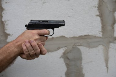 Erkek eli silah tutuyor ve gri duvar arkasına ateş etmeye hazır. Boşluğu kopyala