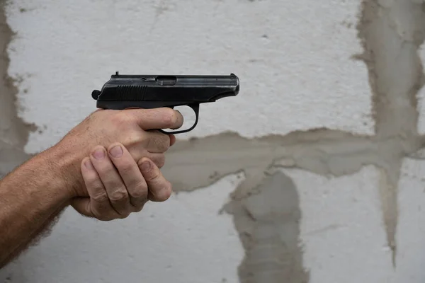 Man hand holds gun and ready to shoot on a grey wall background. copy space