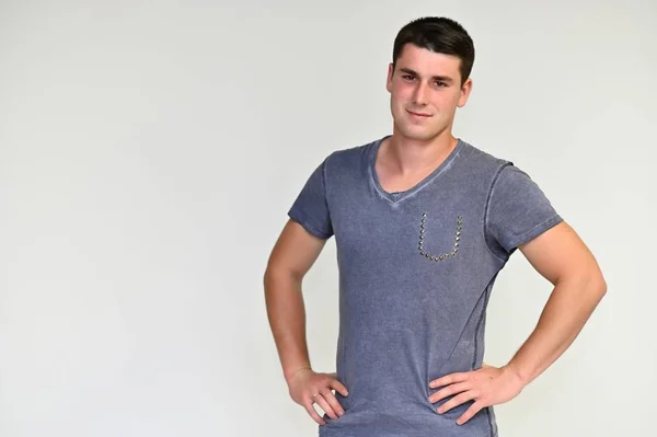 Retrato de um jovem bonito com cabelo preto em uma camiseta azul e cinza em um fundo branco. Mostra emoções em várias poses, falando . — Fotografia de Stock