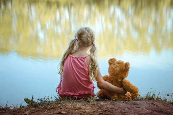 Pequena criança com ursinho sentado juntos visão traseira — Fotografia de Stock