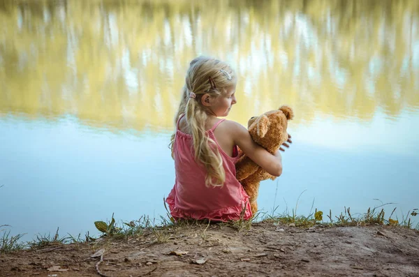 Pequena criança amamentando ursinho de pelúcia enquanto sentado juntos visão traseira — Fotografia de Stock