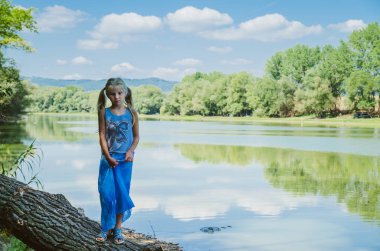 küçük kız ağaç dalları altında nehir kıyısında yürüyüş
