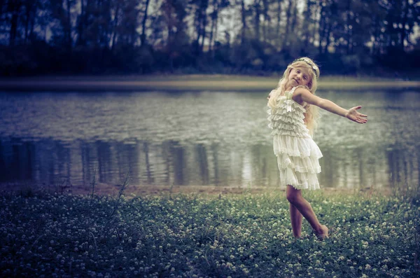 小女孩与长的金发在粉红色的礼服在午夜跳舞在河的绿色草 — 图库照片