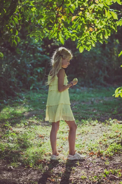 Niña encantadora en vestido amarillo de pie bajo el árbol — Foto de Stock