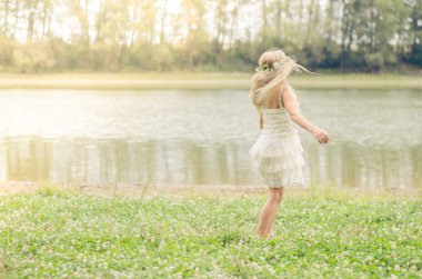 Beyaz elbiseli yeşil çim nehir kenarında dans uzun sarı saçlı küçük kız
