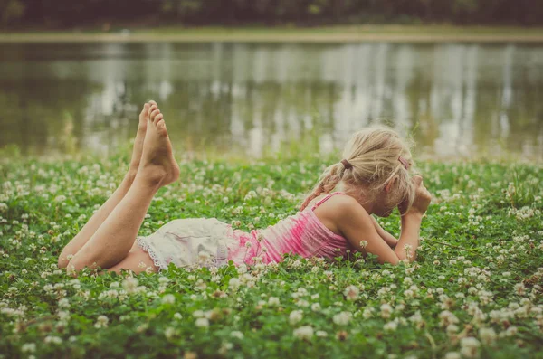 Маленька дитина розслабляється на зеленій траві на березі річки — стокове фото