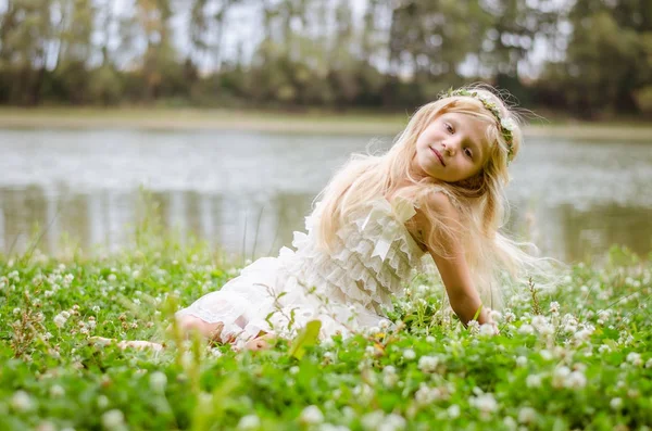 Malá krásná dívka pózuje v trávě u řeky — Stock fotografie
