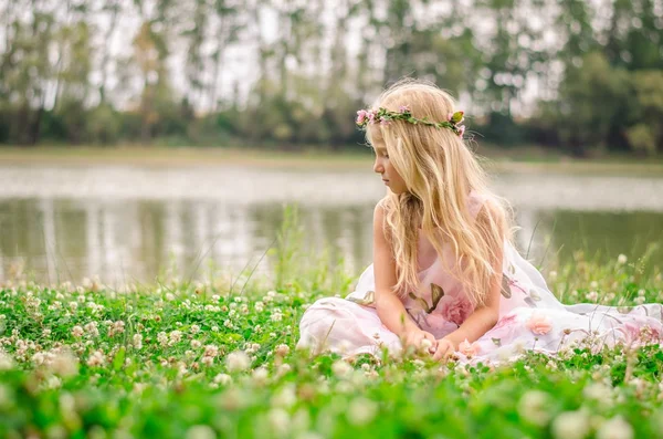 Liten ensam flicka sitter i gräset vid floden — Stockfoto