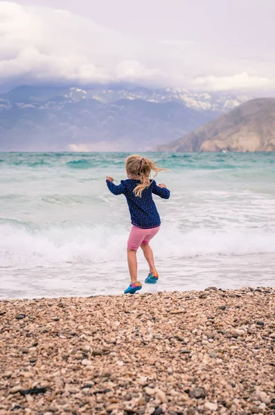 Happy Mała Dziewczynka Skoków Wstecz Zobacz Skalistej Plaży Ciężkich Morze — Zdjęcie stockowe
