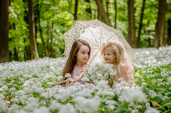 Zwei schöne Kinder sitzen auf der Wiese unter dem Sonnenschirm — Stockfoto