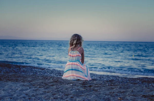 海に海岸の砂で一人で座って長いブロンドの髪を持つ小さな子供 — ストック写真