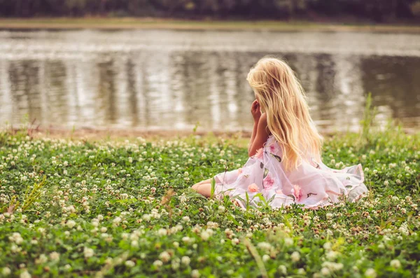 Osamělé dítě sedící v trávě u řeky — Stock fotografie