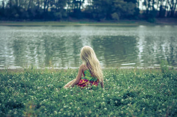 Lille ensom pige sidder i græsset ved floden - Stock-foto