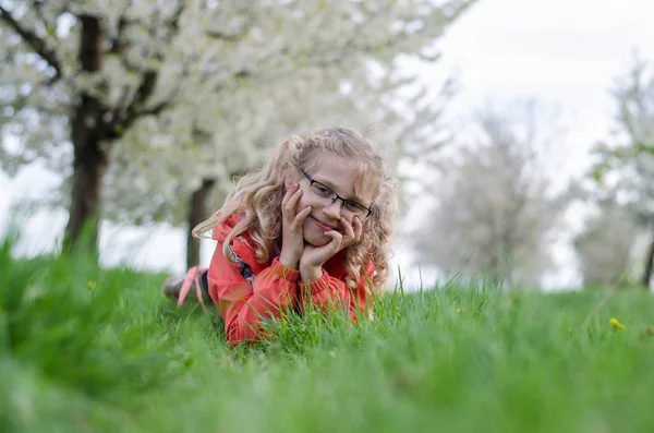 Bedårande Blond Flicka Liggande Gräset Träden Med Blommande Vita Blommor — Stockfoto