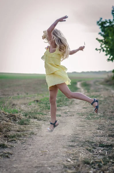 Criança feliz dançando no caminho rural em vestido amarelo — Fotografia de Stock