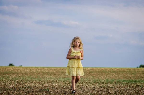 Belle enfant en robe jaune marchant seule et triste dans une belle campagne rurale — Photo