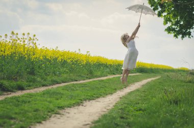 Güzel sarışın kız beyaz güneşlik şemsiyeyle atlıyor.