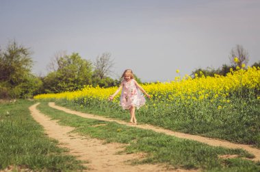 Yeşil doğada kırsal yolda yürüyen yaz elbisesi içindeki küçük sevimli kız.