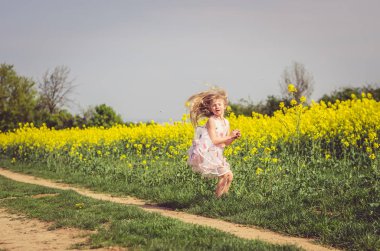 Yeşil doğada kırsal yolda koşan yaz elbisesi içindeki küçük sevimli kız.
