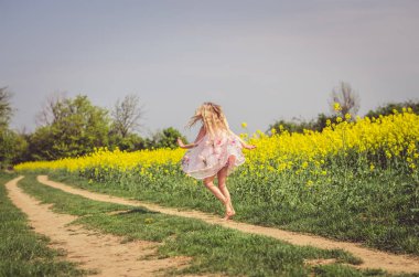 Yeşil doğada kırsal yolda koşan yaz elbisesi içindeki küçük sevimli kız.