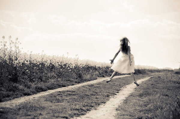 Jumping figure of little girl in white long dress in monochrome countryside