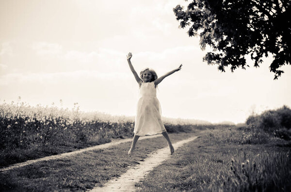 Jumping figure of little girl in white long dress in monochrome countryside