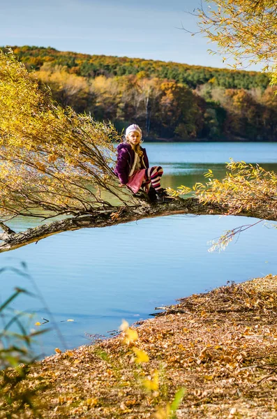 Sonbahar günbatımı atmosferinde ağaçta oturan kız. — Stok fotoğraf