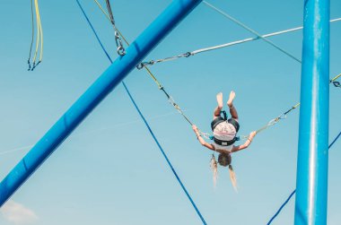 Küçük çocuk bungee jumping 'te eğleniyor. Mavi gökyüzüne doğru yükseliyor.