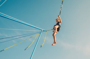 Küçük çocuk bungee jumping 'te eğleniyor. Mavi gökyüzüne doğru yükseliyor.